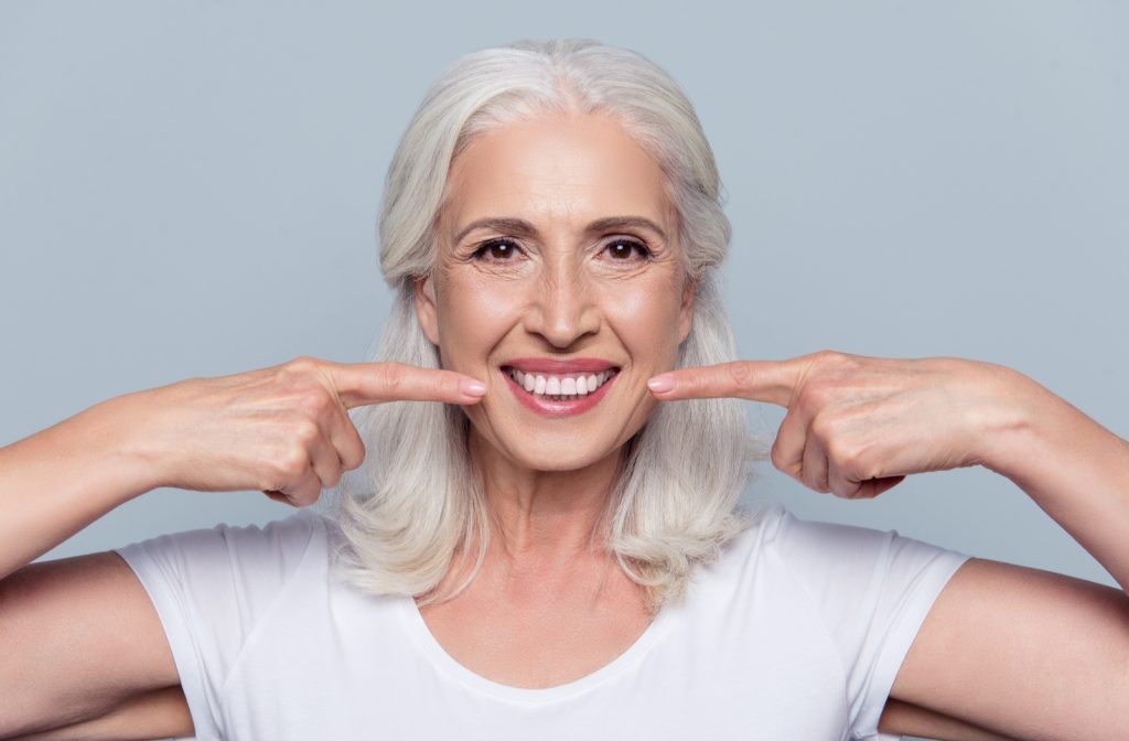 Mature happy woman smiling and pointing at her new set of teeth with both hands.
