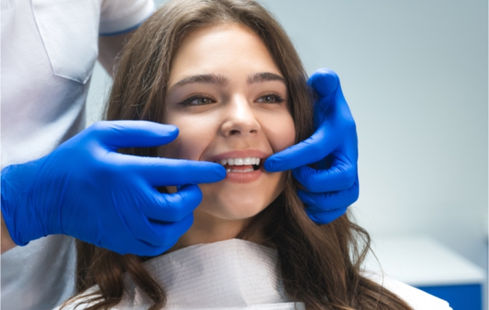Image of a dentist wearing blue gloves examining the teeth of a young female patient after her dental procedure.